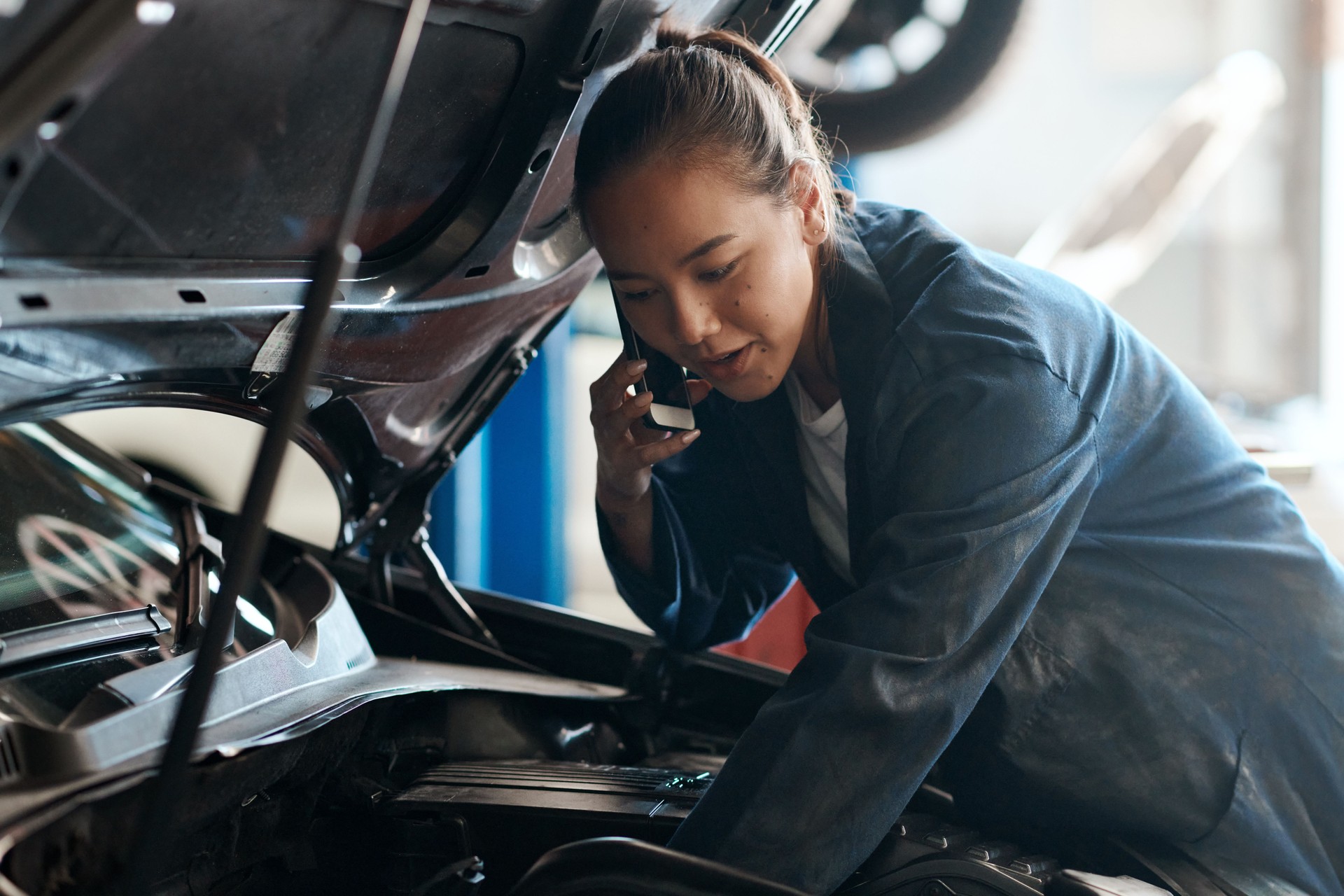 Photo d’une mécanicienne parlant sur son téléphone portable alors qu’elle travaillait dans un atelier de réparation automobile